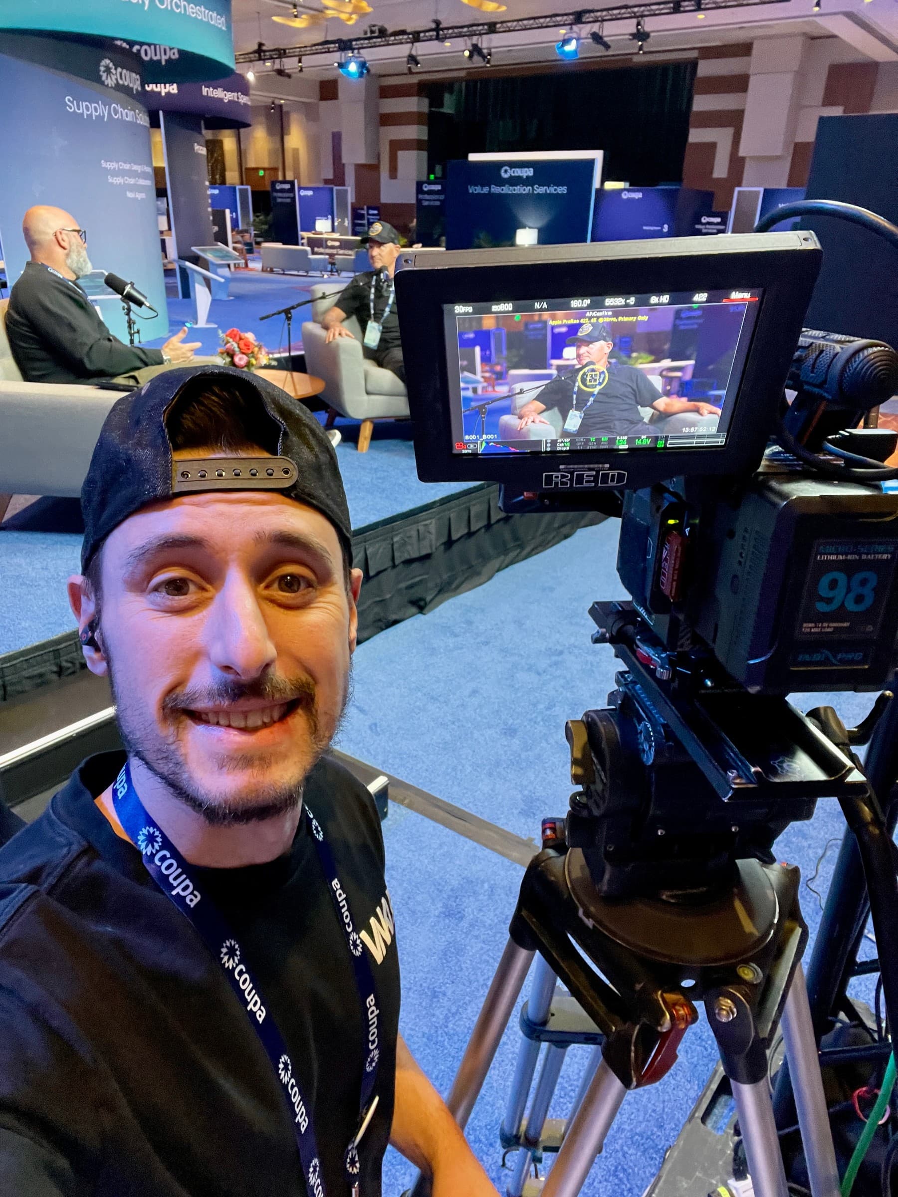Garrett beside a broadcast camera at a conference stage
