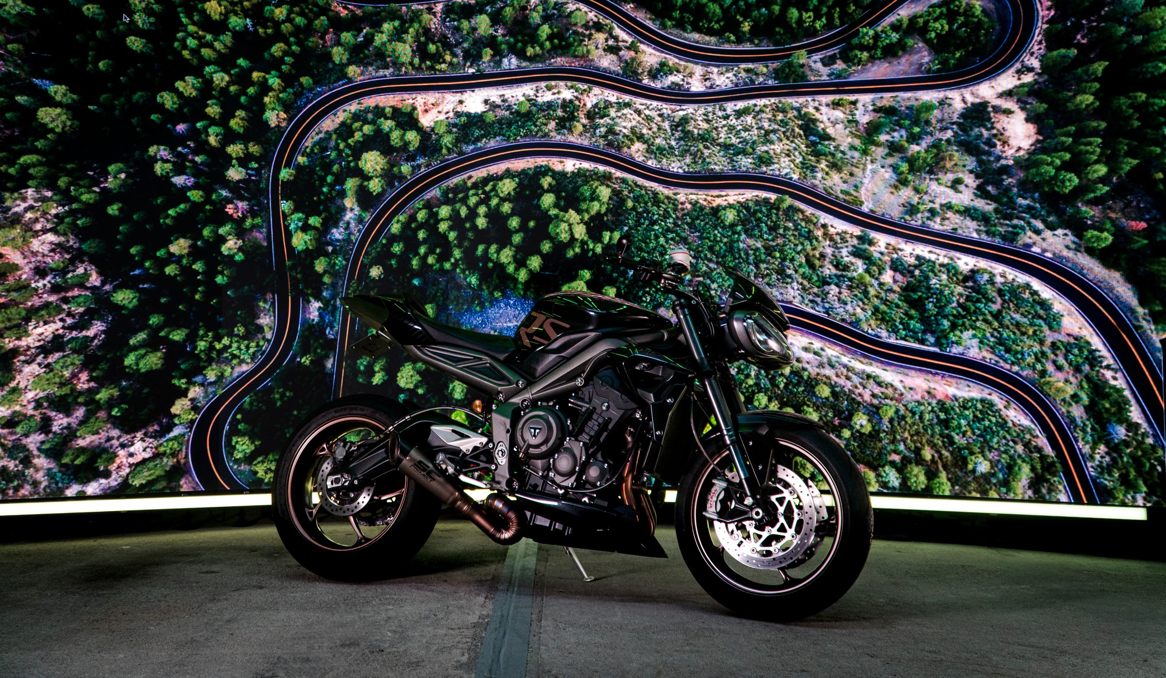 Black street motorcycle on the LED stage in front of an aerial of a winding mountain road