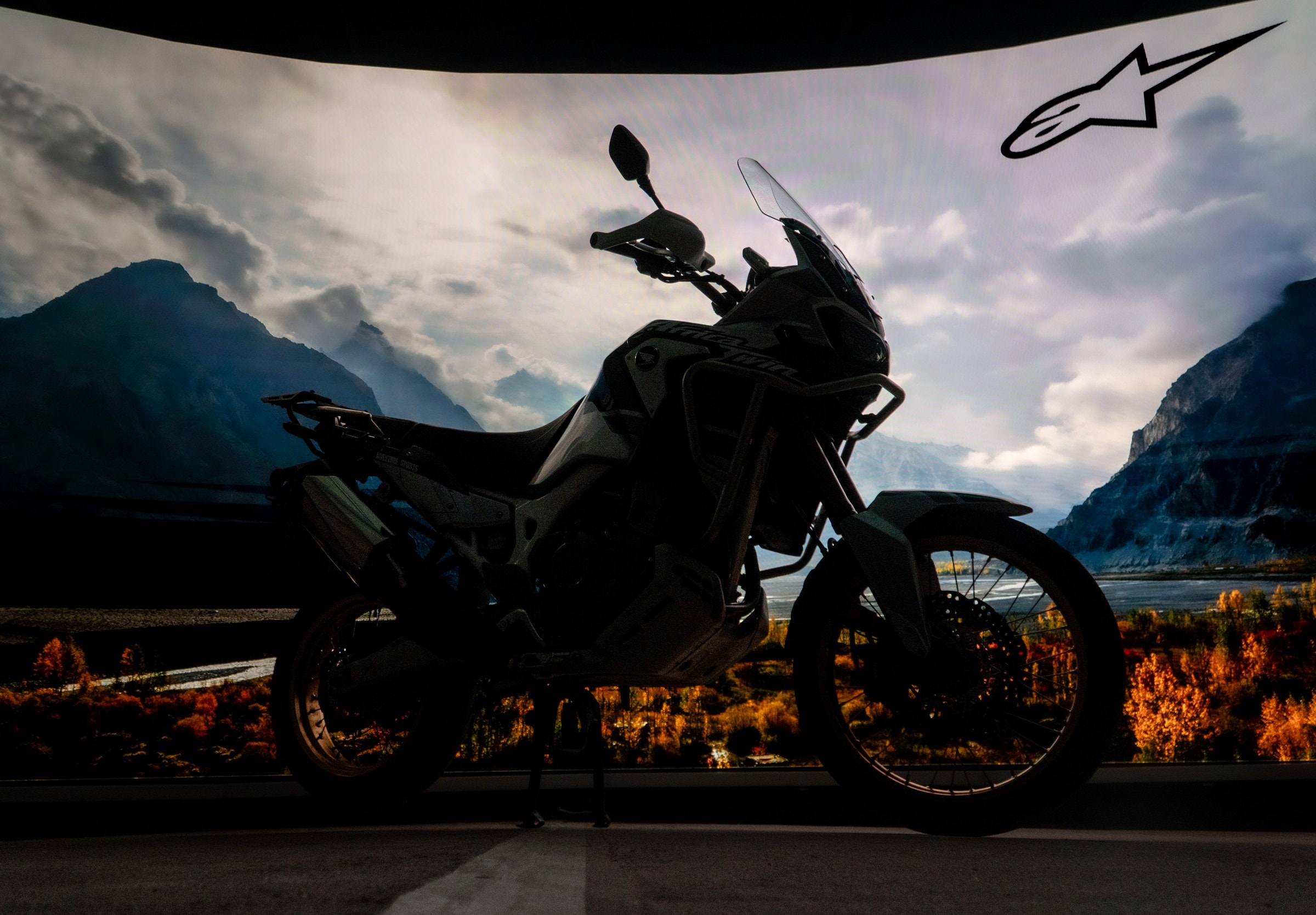 Adventure bike in silhouette against LED mountains under the Alpinestars logo