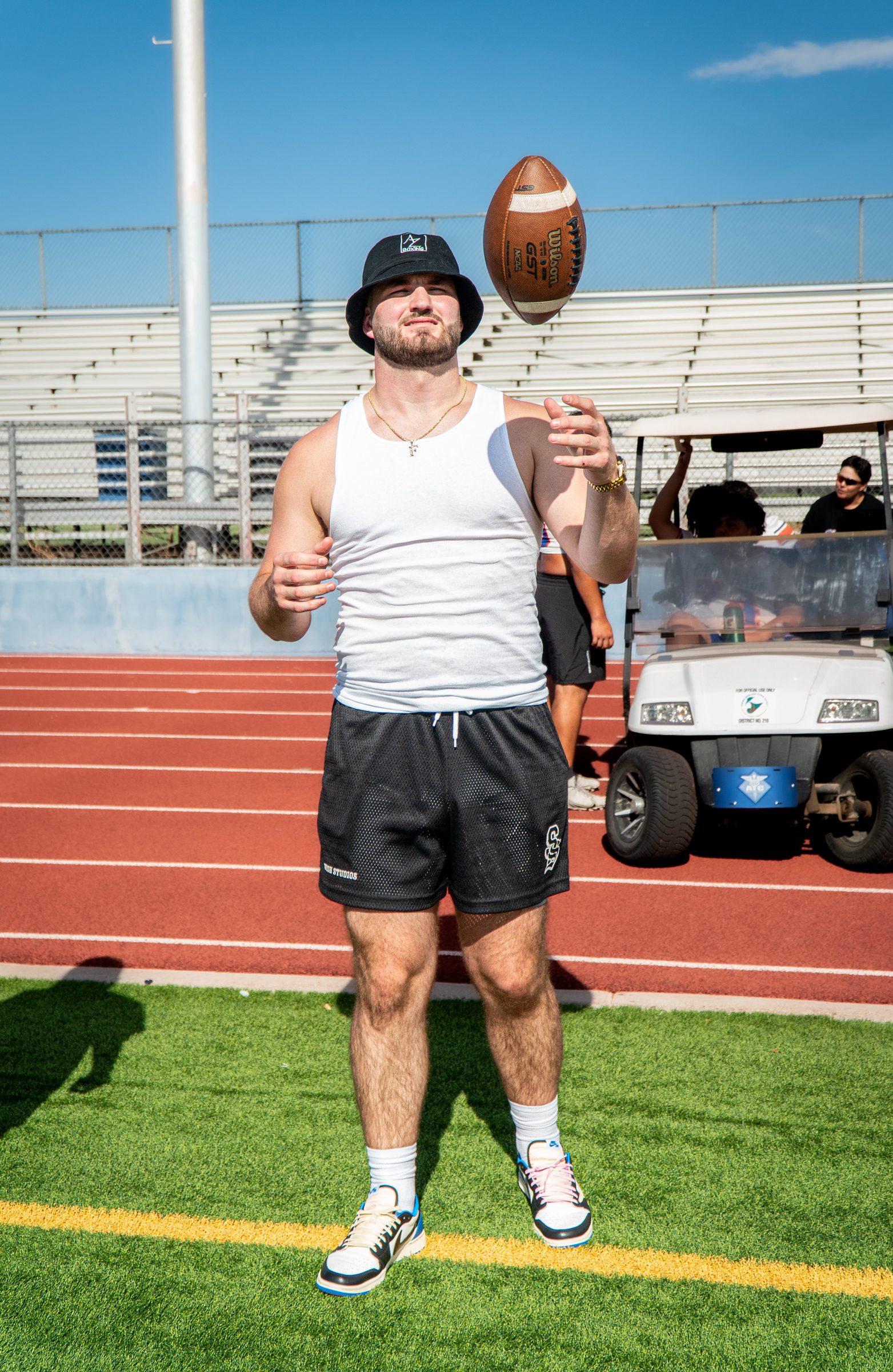 Man in a bucket hat spinning a football on a stadium field