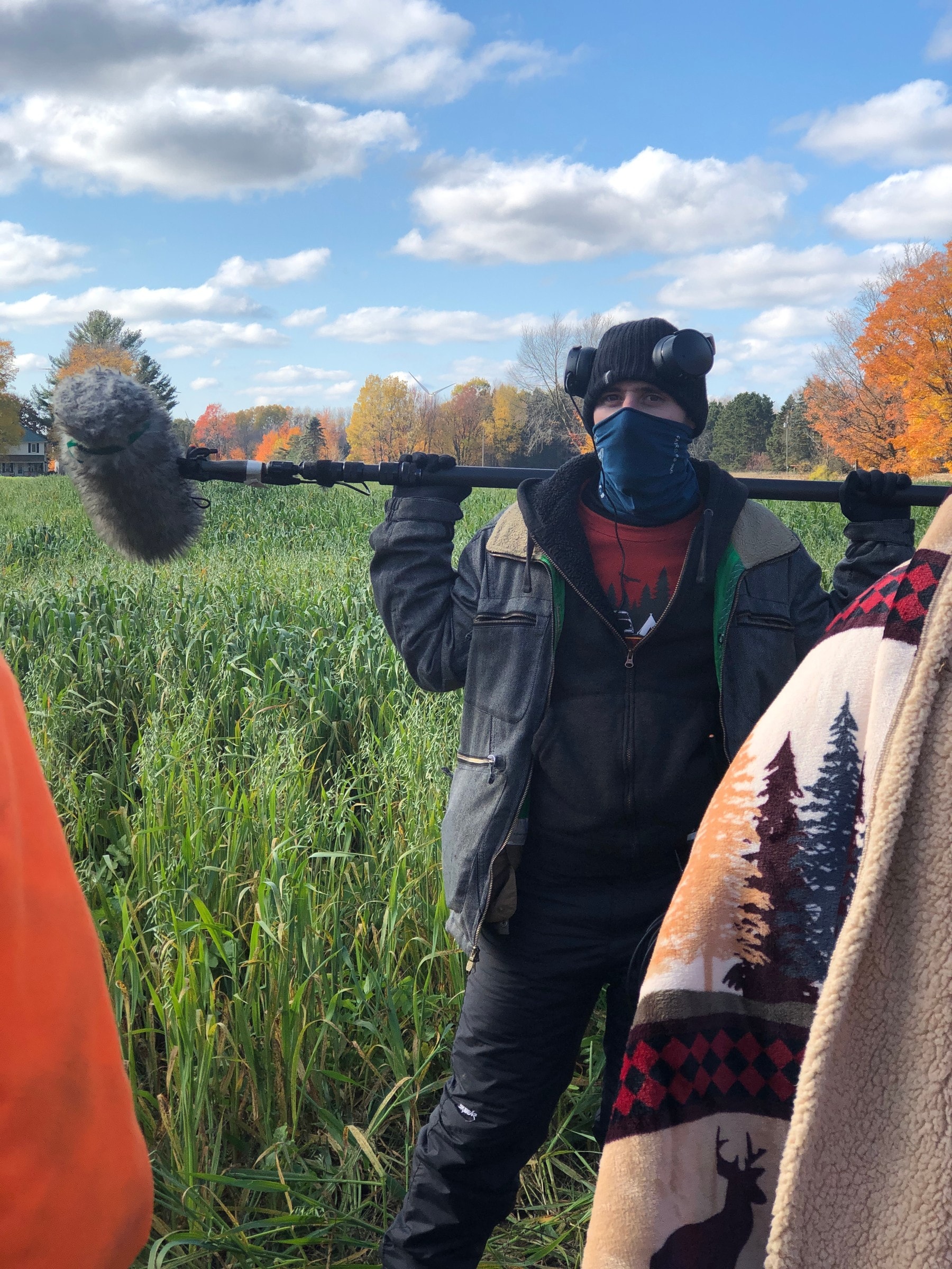 Boom operator with the pole on his shoulder in a Michigan field, fall colors behind