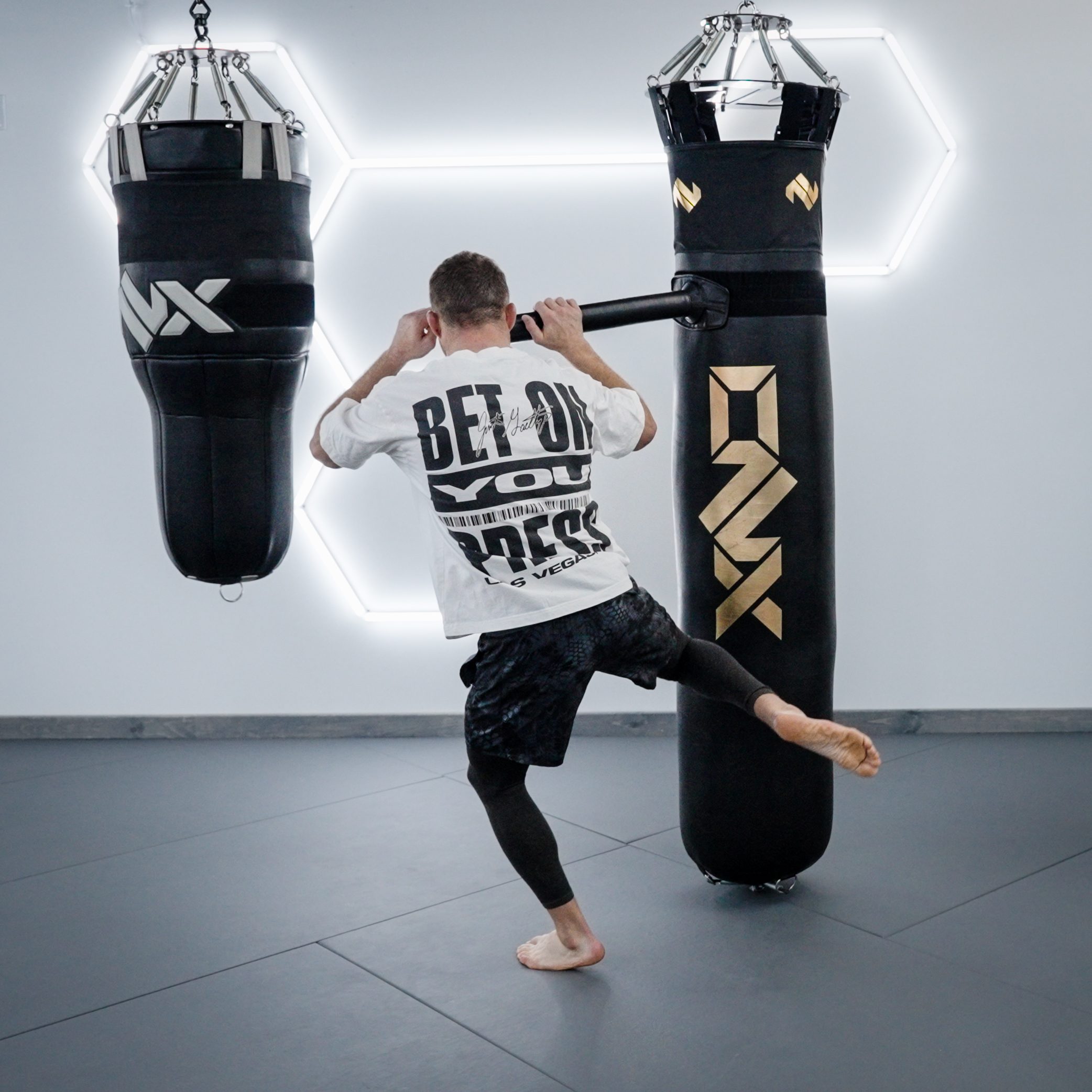 Gaethje throws a knee into a heavy bag in a white "Bet On You" tee
