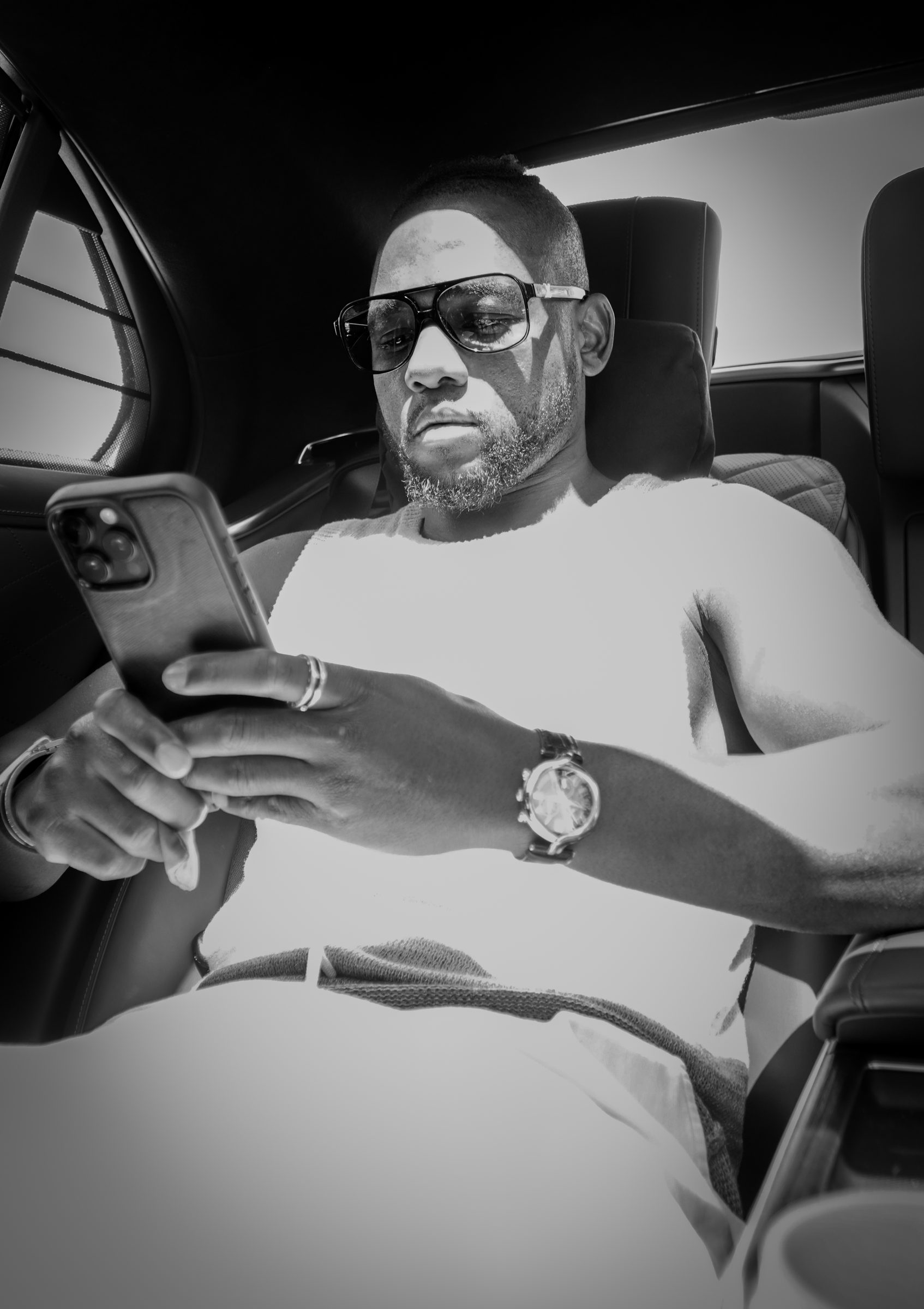 Black and white: Manel Kape checking his phone in the back of a car