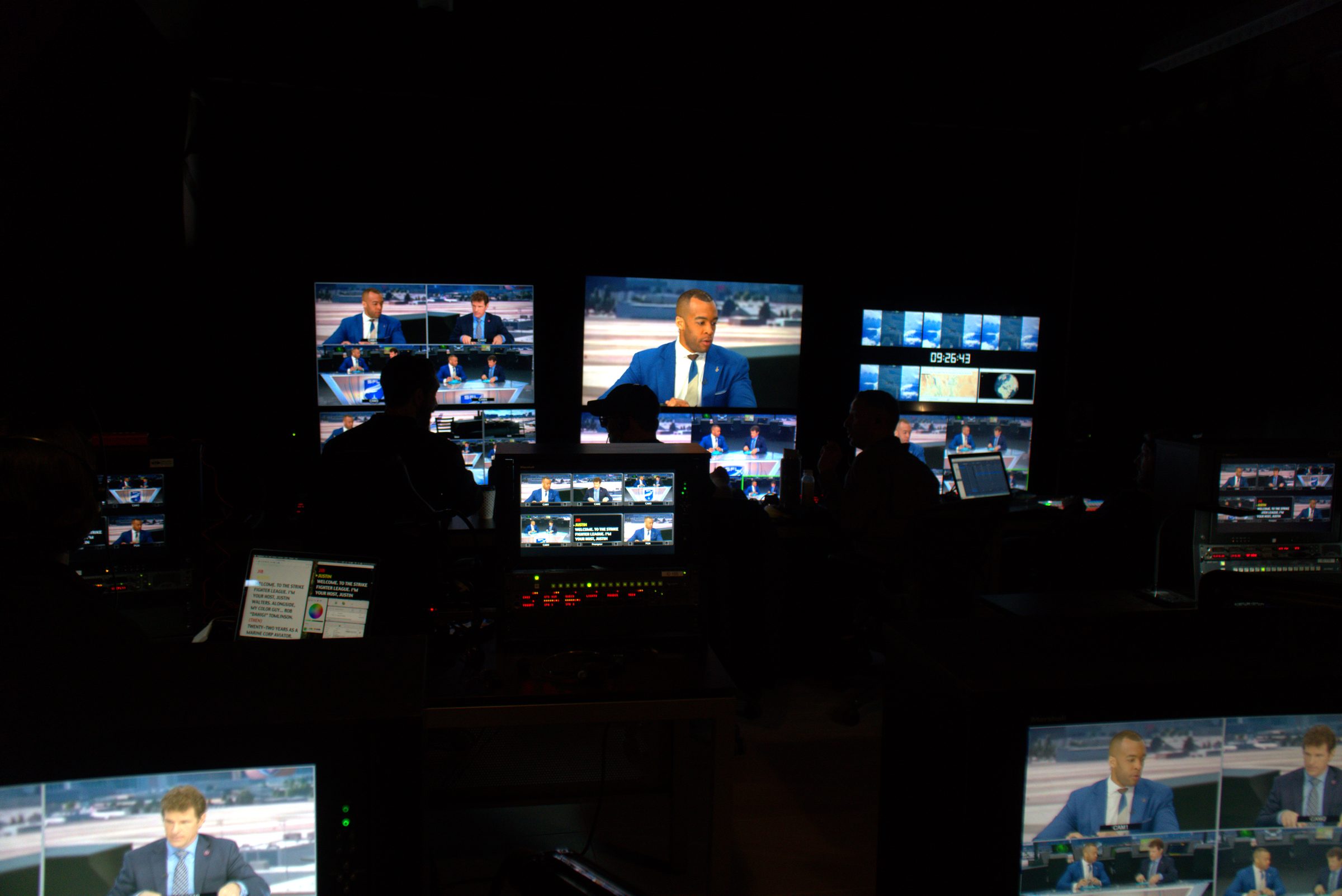 Dark control room lit by a wall of broadcast monitors